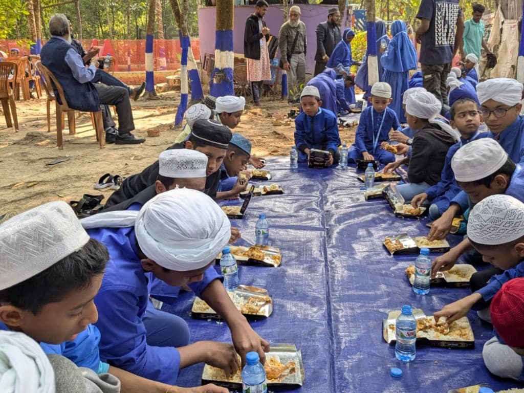 Students seated for a communal meal outdoors on a blue tarp