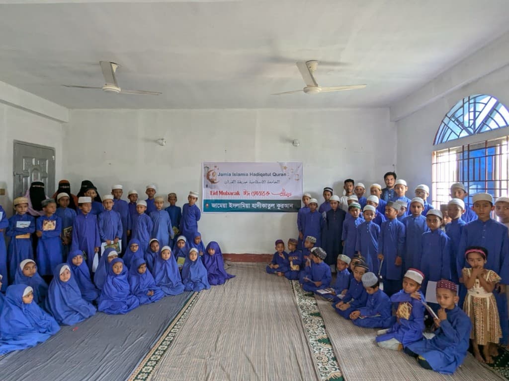 Madrasa students and teachers gathered indoors with an Eid banner